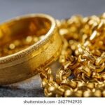 Närbild på en bred guldring och en glittrande guldkedja på en mörk yta.