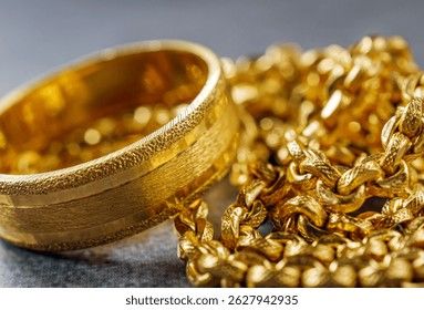 Närbild på en bred guldring och en glittrande guldkedja på en mörk yta.